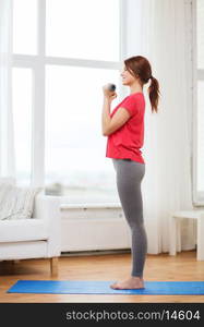 fitness, home and diet concept - smiling redhead girl exercising with heavy dumbbells at home