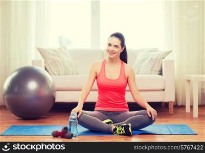 fitness, home and diet concept - smiling teenage girl sitting on mat with sports equipment at home