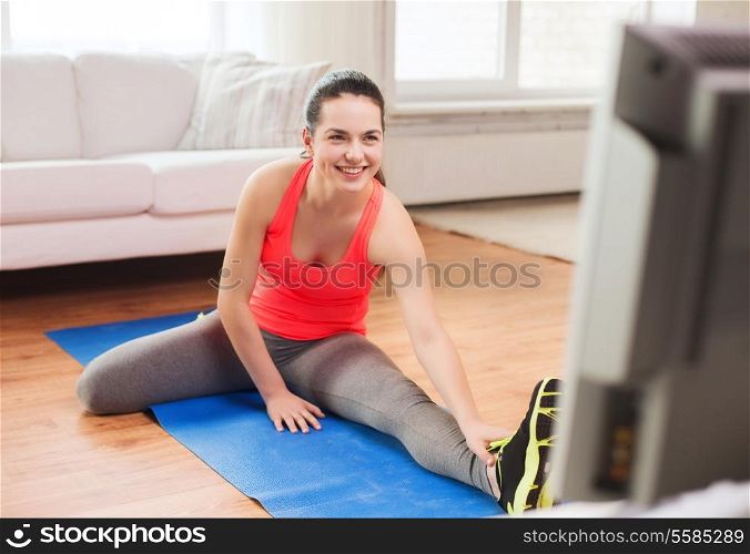 fitness, home and diet concept - smiling teenage girl streching on floor and watching tv at home