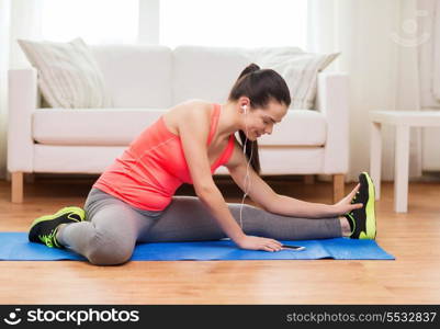 fitness, home, technology and diet concept - smiling teenage girl streching on floor with smartphone and earphones at home