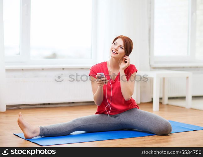 fitness, home, technology and diet concept - smiling teenage girl streching on floor with smartphone and earphones at home