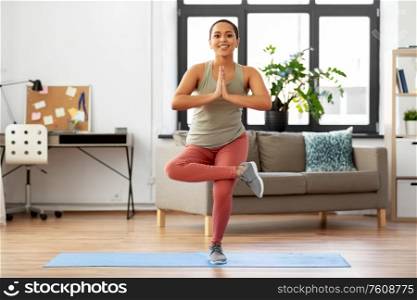 fitness, meditation and healthy lifestyle concept - happy smiling young african american woman doing yoga tree pose at home. african american woman doing yoga pose at home