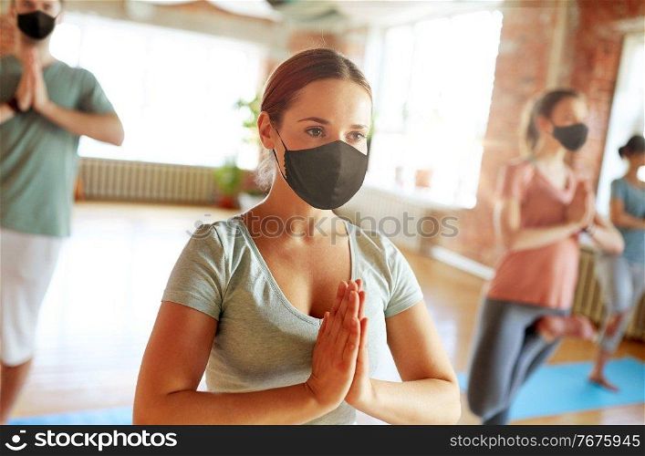 fitness, meditation and healthy lifestyle concept - woman group of people wearing face protective black masks for protection from virus disease doing yoga in tree pose at studio. group of people in masks doing yoga at studio