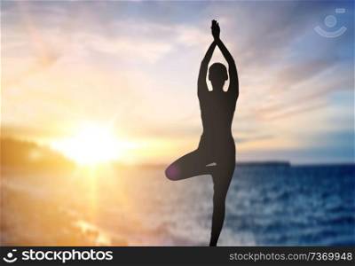 fitness, mindfulness and harmony concept - black silhouette of woman doing yoga tree pose over sunset and sea background. silhouette of woman making yoga over sea sunset