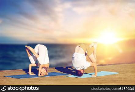 fitness, people and healthy lifestyle concept - couple doing yoga headstand outdoors on wooden pier over sea background. couple doing yoga headstand outdoors