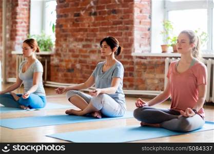 fitness, people and healthy lifestyle concept - group of women meditating in lotus pose at yoga studio. group of women making yoga exercises at studio. group of women making yoga exercises at studio