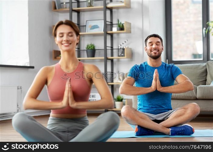 fitness, people and healthy lifestyle concept - happy smiling man and woman meditating in yoga lotus pose at home. happy couple meditating in yoga lotus pose at home