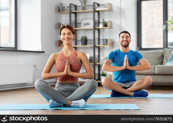 fitness, people and healthy lifestyle concept - happy smiling man and woman meditating in yoga lotus pose at home. happy couple meditating in yoga lotus pose at home