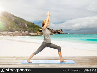 fitness, people and healthy lifestyle concept - happy woman doing yoga warrior pose on mat over exotic tropical beach background. happy woman doing yoga warrior pose on beach