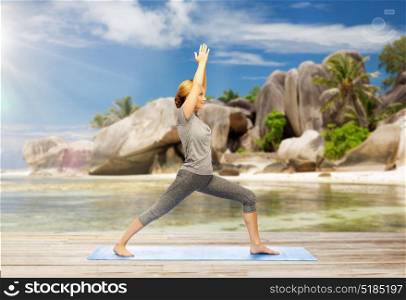 fitness, people and healthy lifestyle concept - happy woman doing yoga warrior pose on mat over exotic tropical beach background. happy woman doing yoga warrior pose on beach