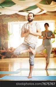 fitness, people and healthy lifestyle concept - man and woman doing yoga in tree pose at studio. man and woman doing yoga tree pose at studio