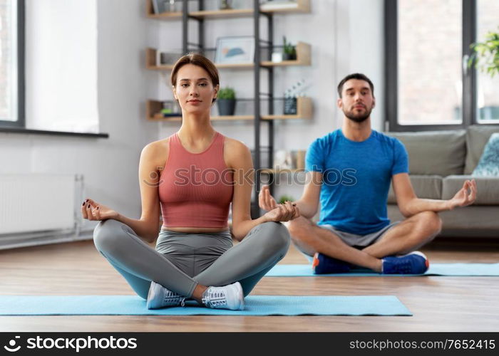 fitness, people and healthy lifestyle concept - man and woman meditating in yoga lotus pose at home. couple meditating in yoga lotus pose at home