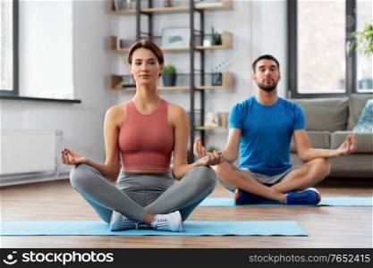 fitness, people and healthy lifestyle concept - man and woman meditating in yoga lotus pose at home. couple meditating in yoga lotus pose at home