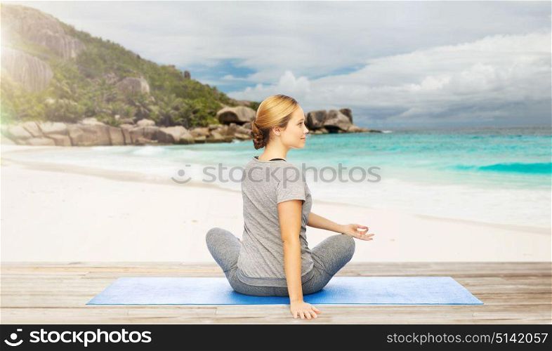 fitness, people and healthy lifestyle concept - woman doing yoga in twist pose on mat over exotic tropical beach background. woman doing yoga in twist pose on beach