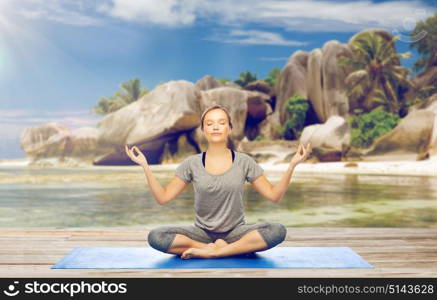 fitness, people and healthy lifestyle concept - woman doing yoga meditation in lotus pose on mat over exotic tropical beach background. woman doing yoga meditation in lotus pose on beach