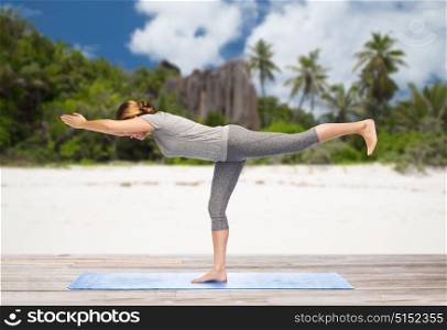 fitness, people and healthy lifestyle concept - woman doing yoga warrior pose on half-bent right leg on mat over exotic tropical beach background. woman doing yoga warrior pose on half-bent outdoor