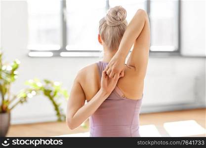fitness, people and healthy lifestyle concept - young woman doing cow face arms pose at yoga studio. woman doing cow face arms pose at yoga studio
