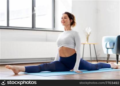 fitness, people and healthy lifestyle concept - young woman doing splits yoga pose at studio. young woman doing splits yoga pose at studio