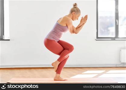 fitness, people and healthy lifestyle concept - young woman doing yoga in eagle pose at studio. young woman doing yoga eagle pose at studio