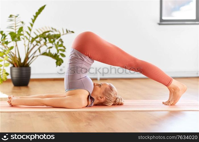 fitness, people and healthy lifestyle concept - young woman doing yoga in plow pose at home. woman doing yoga in plow pose at home