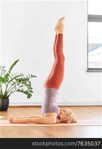 fitness, people and healthy lifestyle concept - young woman doing yoga in supported shoulderstand at home. woman doing yoga in shoulderstand at home