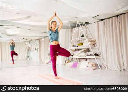 fitness, people and healthy lifestyle concept - young woman doing yoga in tree pose at studio. young woman doing yoga tree pose at studio