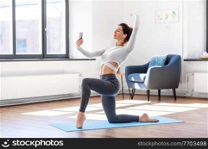 fitness, people and healthy lifestyle concept - young woman with smartphone and earphones doing yoga at home. young woman with smartphone doing yoga at home
