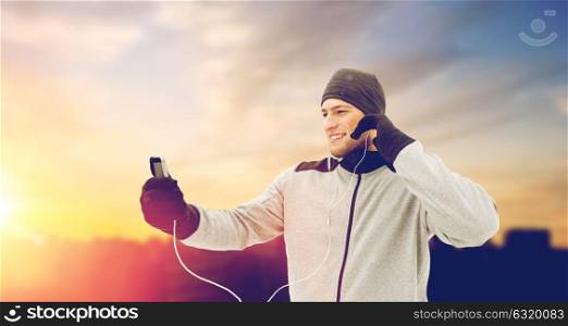 fitness, people and technology concept - happy smiling young man in earphones with smartphone listening to music outdoors. happy man with earphones and smartphone in winter