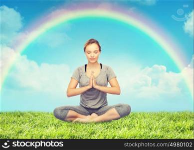 fitness, people, harmony and healthy lifestyle concept - woman making yoga meditation in lotus pose over grass and rainbow in blue sky background. woman meditating in lotus yoga pose over rainbow