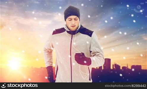 fitness, people, technology and healthy lifestyle concept - young man in earphones with smartphone listening to music and running in city. happy man with earphones and smartphone in winter