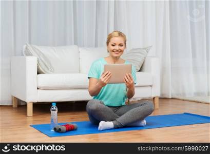 fitness, people, technology, exercising and sport concept - smiling woman with tablet pc computer and dumbbells sitting on mat at home