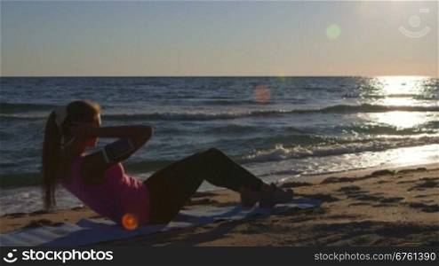 Fitness routine for women - athletic girl doing abdominal crunch on the beach