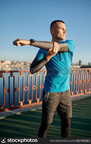 Fitness runner doing warm-up routine before speed running. Man stretching arms muscles preparing for cardio workout fast jogging. Closeup view. Fitness runner doing warm-up routine before speed running