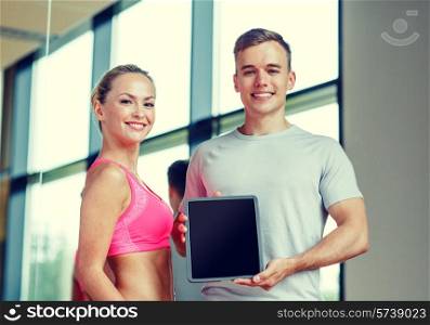 fitness, sport, advertising, technology and diet concept - smiling young woman and personal trainer with tablet pc blank screen in gym