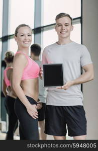 fitness, sport, advertising, technology and diet concept - smiling young woman and personal trainer with tablet pc blank screen in gym