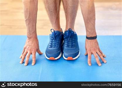 fitness, sport and footwear concept - close up of male hands and feet in blue sneakers on exercise mat. close up of male hands and feet on exercise mat
