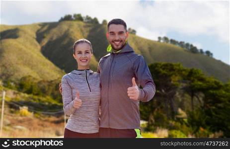 fitness, sport and gesture concept - smiling couple outdoors showing thumbs up over big sur hills background in california. smiling couple in sport clothes showing thumbs up. smiling couple in sport clothes showing thumbs up
