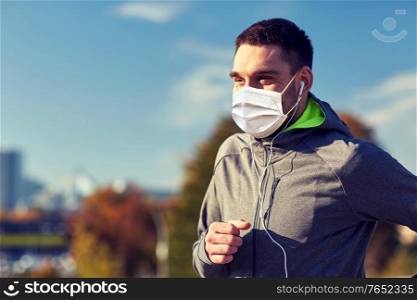 fitness, sport and health concept - man wearing face protective medical mask for protection from virus disease running and listening to music in earphones at city. man in mask with earphones running in city