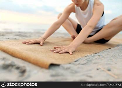fitness, sport, and healthy lifestyle concept - close up of woman doing yoga stretching pose on beach over sunset. woman doing yoga stretching pose on beach