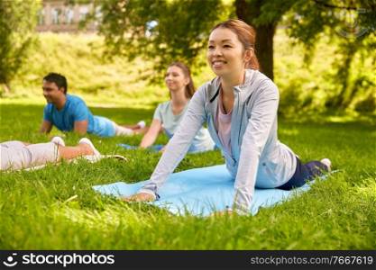 fitness, sport and healthy lifestyle concept - group of happy people doing yoga full cobra pose at summer park. group of people doing yoga at summer park