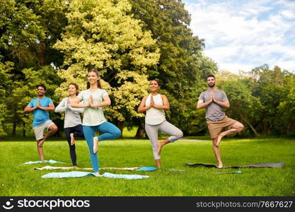 fitness, sport and healthy lifestyle concept - group of happy people doing yoga at summer park. group of people doing yoga at summer park