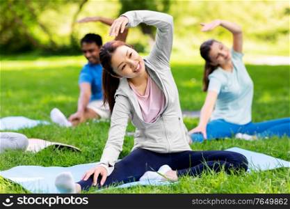 fitness, sport and healthy lifestyle concept - group of happy people exercising at summer park. group of people exercising at summer park