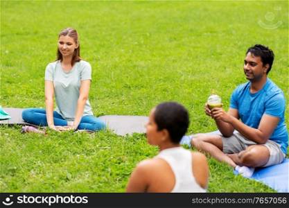 fitness, sport and healthy lifestyle concept - group of happy people sitting on yoga mats at park. group of people sitting on yoga mats at park