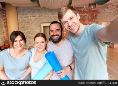 fitness, sport and healthy lifestyle concept - group of happy people with mats at yoga studio or gym taking selfie. happy friends at yoga studio or gym taking selfie. happy friends at yoga studio or gym taking selfie
