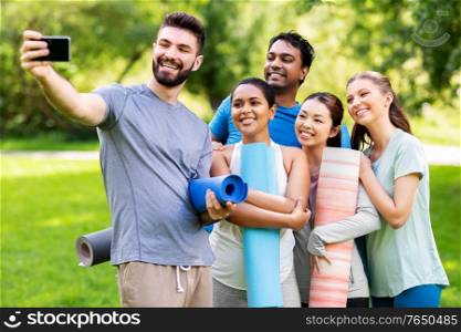 fitness, sport and healthy lifestyle concept - group of happy people with yoga mats taking selfie at park. happy people with yoga mats taking selfie at park