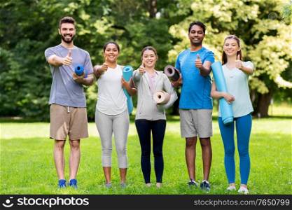 fitness, sport and healthy lifestyle concept - group of happy people with yoga mats showing thumbs up at park. people with yoga mats showing thumbs up at park