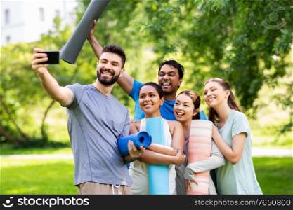 fitness, sport and healthy lifestyle concept - group of happy people with yoga mats taking selfie at park. happy people with yoga mats taking selfie at park