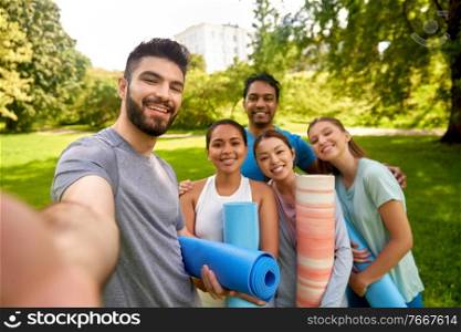 fitness, sport and healthy lifestyle concept - group of happy people with yoga mats taking selfie at park. people with yoga mats taking selfie at park