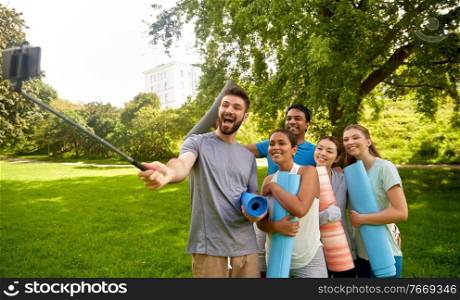 fitness, sport and healthy lifestyle concept - group of happy people with yoga mats taking selfie with smartphone at park. people with yoga mats taking selfie at park