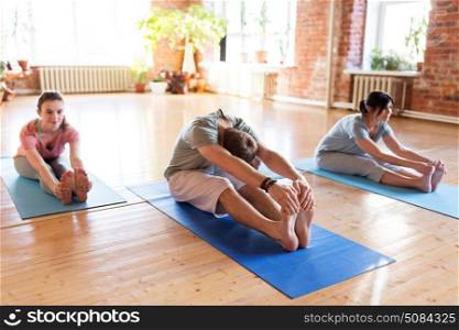 fitness, sport and healthy lifestyle concept - group of people doing yoga seated forward bend pose on mats at studio. group of people doing yoga forward bend at studio. group of people doing yoga forward bend at studio